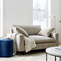 a living room with a couch, ottoman and coffee table in front of a window