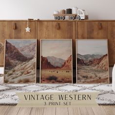 three vintage western prints are on display in front of a wooden cabinet with baskets and coffee mugs