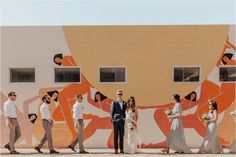 a group of people standing in front of a wall painted with orange and white designs