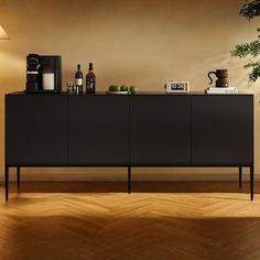 a sideboard with drinks on it in front of a potted plant and lamp