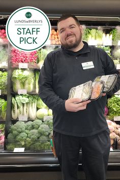 a man standing in front of a produce stand holding a bag full of fresh vegetables