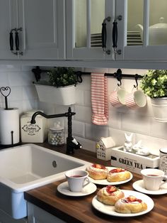 a kitchen counter with plates and cups on it next to a sink, potted plants and teapots