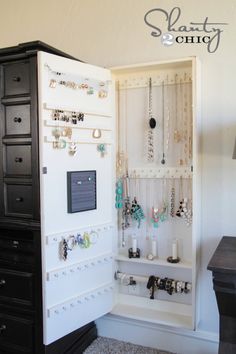 a jewelry cabinet is open to show necklaces and bracelets on the wall above it