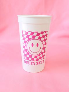 a pink and white checkered cup with a smiley face in the middle on a pink background