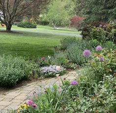 a garden filled with lots of flowers next to a lush green park covered in trees