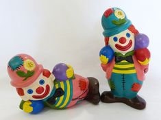 two ceramic clowns sitting next to each other on a white surface with one laying down