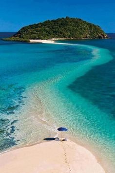 an island in the middle of blue water next to white sand beach with umbrellas on it