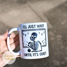 a person holding a coffee mug with a skeleton on it that says, i'll just wait until it's quiet