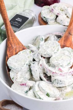 a white bowl filled with cucumber salad on top of a table next to two wooden spoons