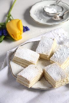 several pieces of cake on a plate with flowers and teacups in the background