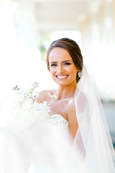 a woman in a wedding dress holding a bouquet of flowers and smiling at the camera