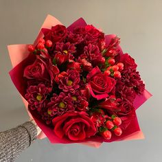 a bouquet of red flowers is held by a woman's hand in front of a gray wall