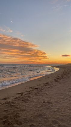 the sun is setting at the beach with footprints in the sand