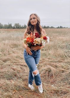 a woman standing in the middle of a field with flowers on her chest and one arm behind her back