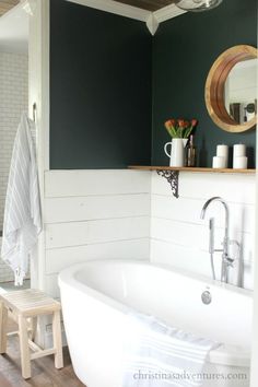 a white bath tub sitting in a bathroom next to a wooden stool and wall mounted mirror