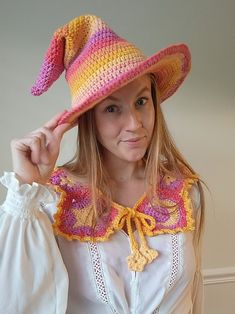 a woman wearing a pink and yellow crochet hat holding her hand up to her face