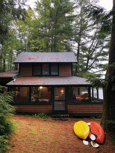 a house in the woods with kayaks on the ground next to it and trees