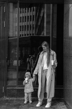 a black and white photo of a woman holding the hand of a child in front of a building