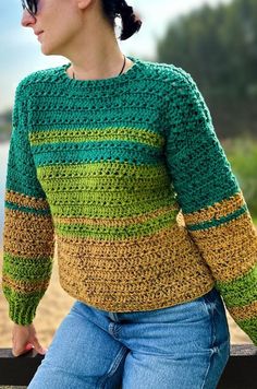 a woman sitting on top of a wooden bench wearing a green and yellow knitted sweater