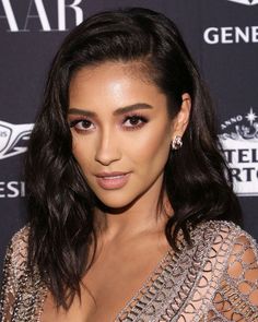 a woman with long dark hair wearing a silver dress and diamond earrings, posing for the camera