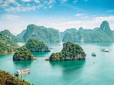 several boats floating in the water near small islands and mountains with green trees on either side