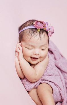 a baby wrapped in a pink blanket with a flower on it's head and smiling