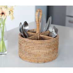 a wicker basket with forks and spoons in it next to a vase filled with daisies