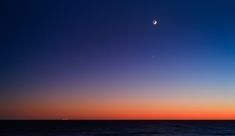 the sun is setting over the ocean with a small boat in the distance