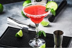 a red cocktail with limes and sugar on the rim, next to utensils