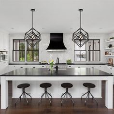 a large kitchen with white cabinets and black counter tops, an island in the center is flanked by three stools