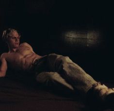 a shirtless man laying on a bed in the dark with his head turned to the side