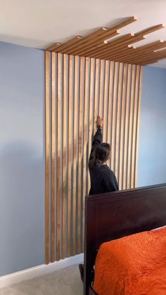 a person standing on top of a bed next to a wooden slatted wall