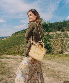 a woman in a floral dress carrying a wicker basket on her shoulder and looking off into the distance