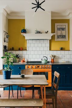 a kitchen with yellow and blue cabinets, an island table and two wooden chairs in front of the stove