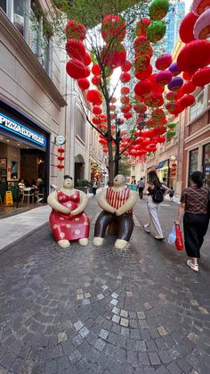 people walking down the street with red and white balloons hanging from the ceiling above them