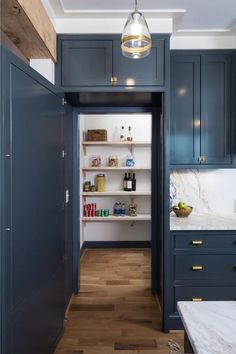 an open pantry with blue cabinets and white marble counter tops, along with wooden flooring