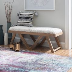 a wooden bench sitting on top of a rug next to a vase filled with flowers