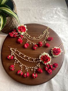 a wooden plate with red flowers and pearls on it next to a potted plant