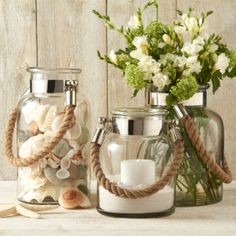 two glass jars with rope handles holding candles and seashells