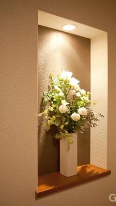 a vase filled with white flowers sitting on top of a wooden shelf next to a mirror