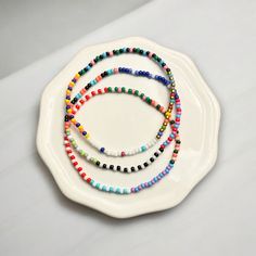 Add a touch of charm to your everyday look with our handcrafted Seed Bead Bracelets. Delicately made with tiny 2mm beads, they're the perfect lightweight accessory for layering up and creating your own style statement -- all without any bulk! Each bracelet is a little piece of art, featuring a delightful mix of colors and designs. And if you're looking for something just for you, we'd love to make it happen! Simply pick your favorite hues from our color chart, and we'll tailor it to your taste. These bracelets are strung on top-notch elastic bead cord for a snug, comfy fit. Plus, they come in a cute cotton pouch with the Georgia Goddess seal, ready to be the perfect gift or a special treat for yourself. *Note From Jess* I personally wear these bracelets for weeks at a time. Waterproof, swe 2mm Bead Bracelet Ideas, Friendship Bracelets With Spacer And Round Beads, Everyday Multicolor Beaded Chain Bracelets, Minimalist Beaded Bracelet With Letter Beads, Minimalist Beaded Necklace With Letter Beads, Minimalist Beaded Necklace With Round Letter Beads, Adjustable Tiny Beads Necklace For Everyday, Minimalist Beaded Chain Bracelets, Everyday Tiny Bead Bracelets