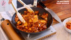 a person cooking food in a skillet on top of a stove with tongs