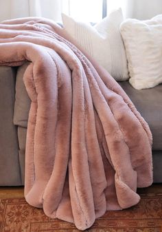 a couch with a pink blanket on top of it next to pillows and a rug