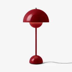 a red table lamp on a white surface with a cord plugged in to it