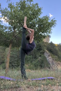 a man doing yoga in the middle of a field with trees and mountains behind him