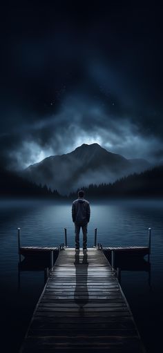 a man standing on a pier looking at the water with mountains in the background and clouds