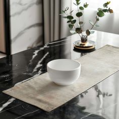 a white bowl sitting on top of a table next to a vase filled with flowers