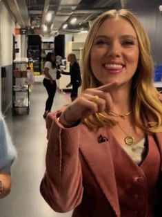 a woman is smiling and pointing to the side in an office hallway with other people