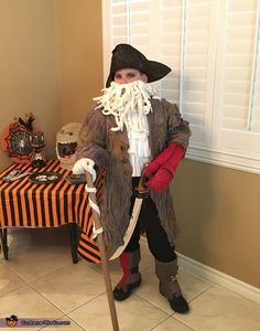 a man dressed up as a pirate with a long white beard and mustache, standing in front of a table