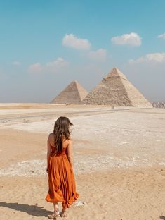 a woman in an orange dress looking at the pyramids